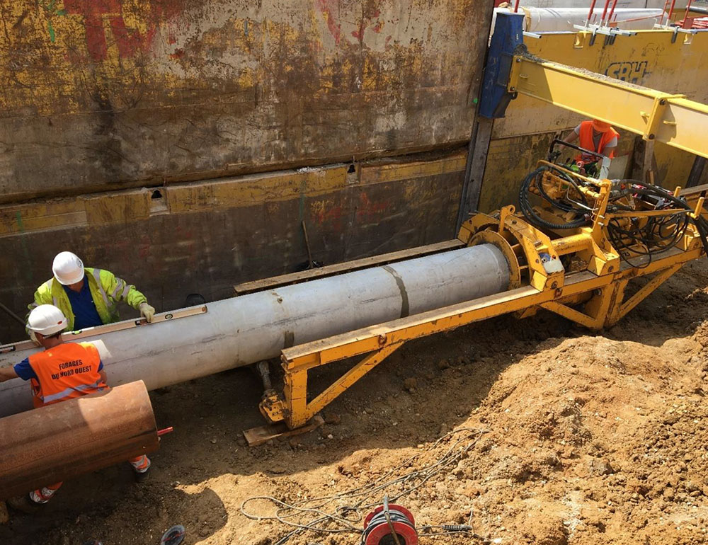 Équipe d'ingénieurs et techniciens opérant une machine de fonçage horizontal pour la pose d'une canalisation en béton dans un puits blindé.